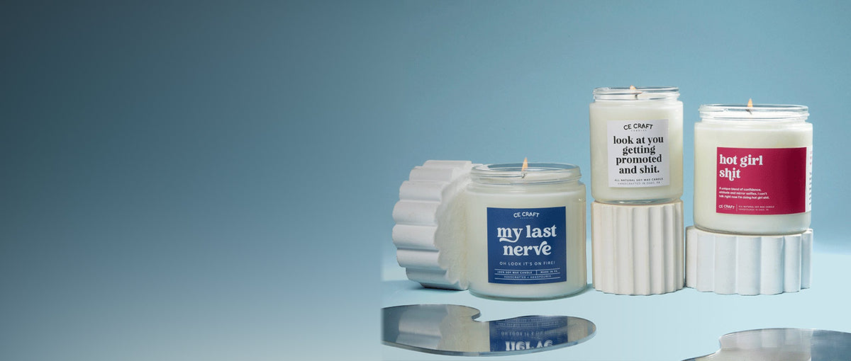 Three C&E candles on white stands against a soft blue backdrop
